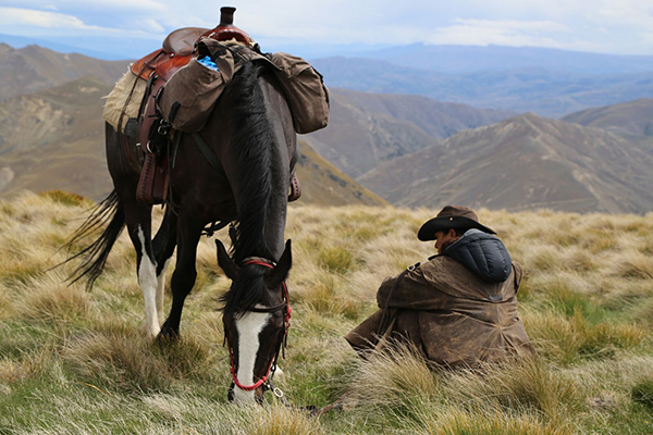 a guest takes a break from horseback riding and sits by his horse in New Zealand hosted by Adventure Horse Trekking