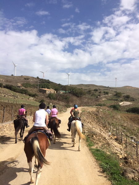 equestrians ride through a village in sicily