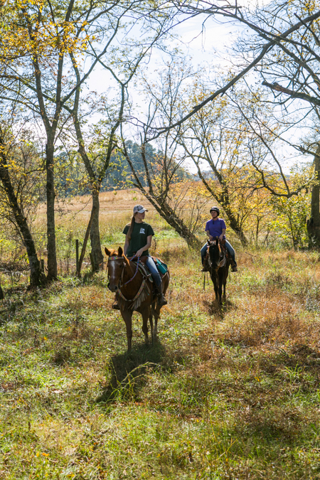 two women ride horses through fall trees in alabama