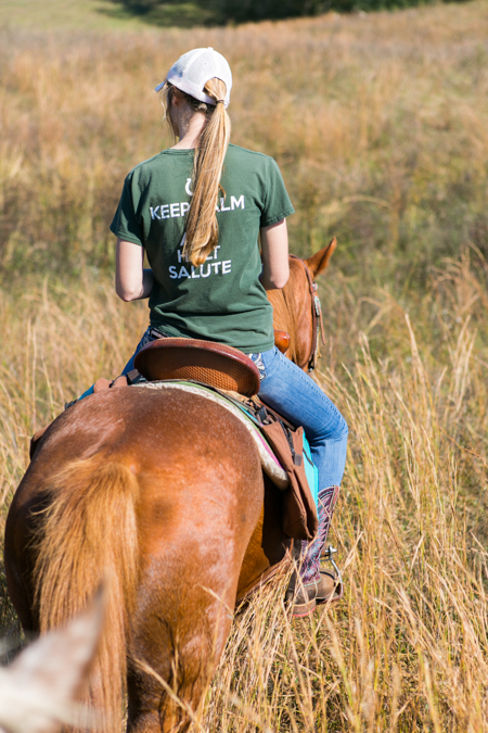 young woman rides horse through tall grass