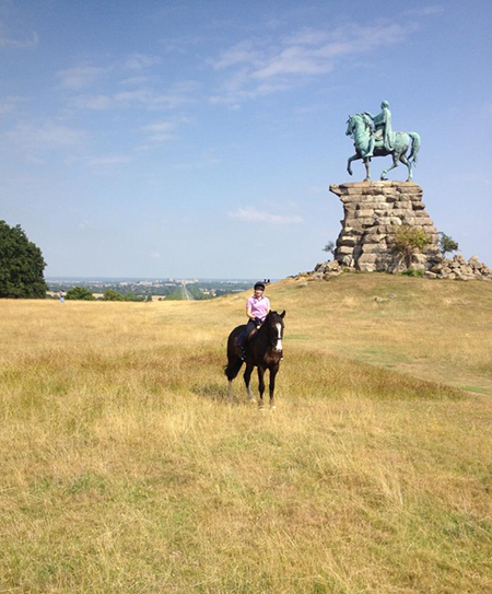 woman riding horse atop snow hill near king george the third statue in windsor great park