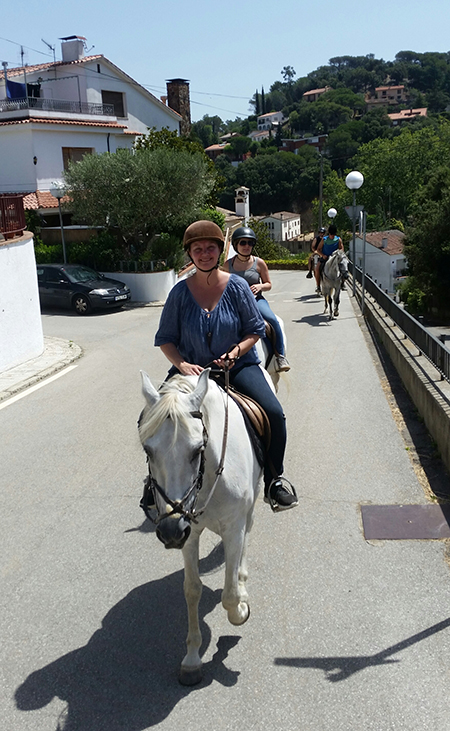 woman riding white andalusian horse through streets of orrius spain